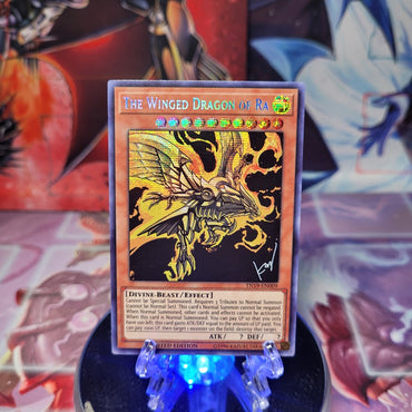A Prismatic Secret Rare "The Winged Dragon of Ra" card from the Yugioh 2019 Gold Sarcophagus Mega-Tins (TN19).